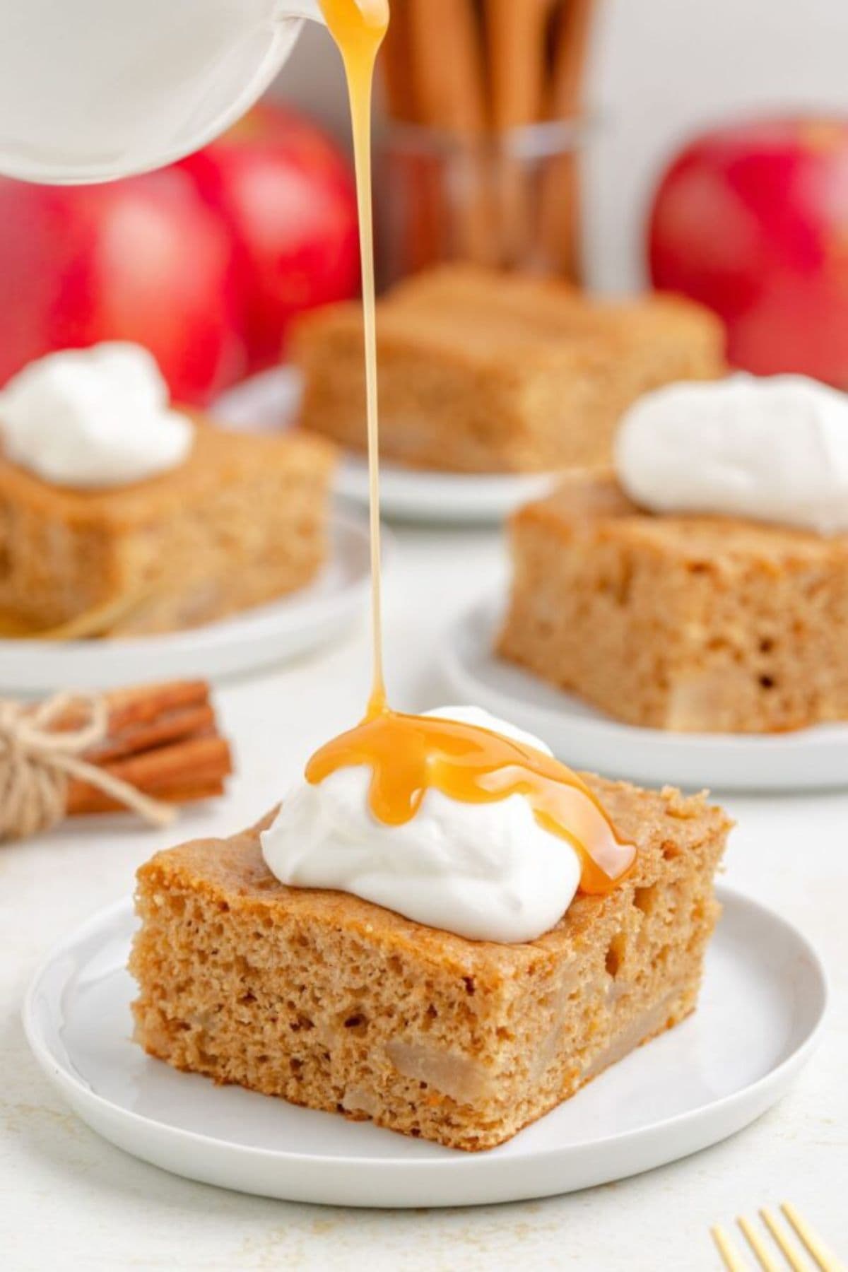 A caramel drizzle pours over whipped cream on a slice of apple cake.