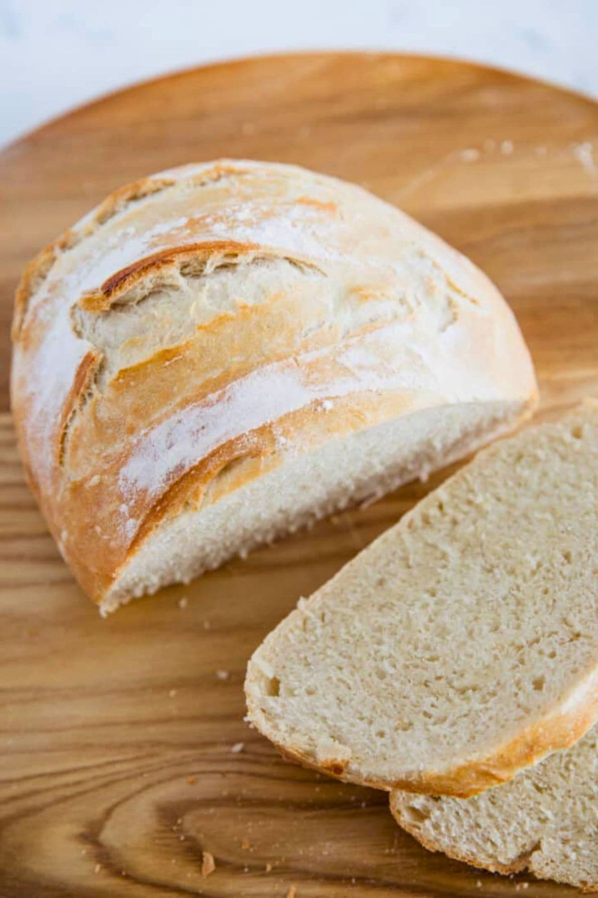 A round loaf of bread with two slices cut on a wooden board.