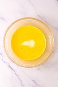 Glass bowl with yellow liquid mixture on a marble surface.