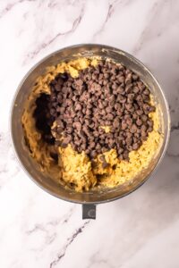 A mixing bowl with cookie dough and chocolate chips on a marble surface.
