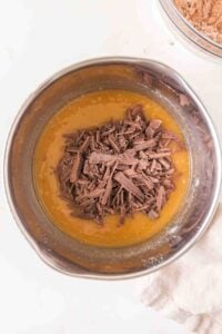Chopped chocolate pieces on top of melted butter in a mixing bowl.