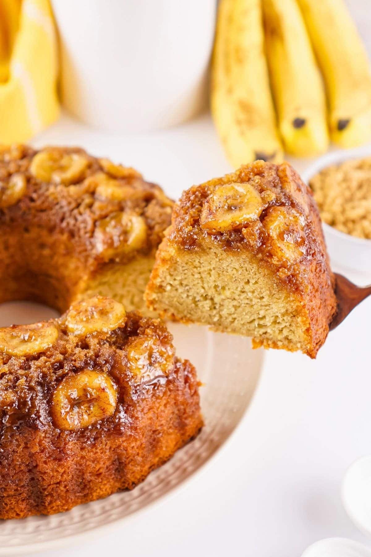A slice of banana upside-down cake being served, with bananas in the background.