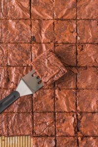 A spatula lifts a fudgy, sliced brownie from a tray of brownies.