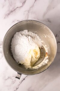 Metal bowl with cream cheese, powdered sugar, and vanilla on a marble surface.