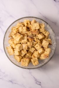 A glass bowl filled with creamy, cubed bread on a marble surface.