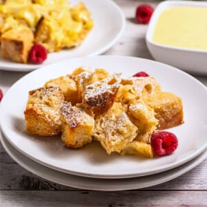 French toast casserole topped with powdered sugar and raspberries on a white plate.