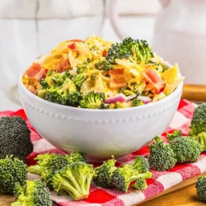 A bowl of broccoli salad with bacon and cheese on a red checkered cloth.