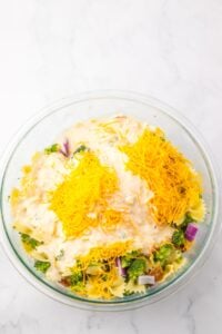 Glass bowl with pasta, broccoli, onions, cheese, and creamy sauce on top.