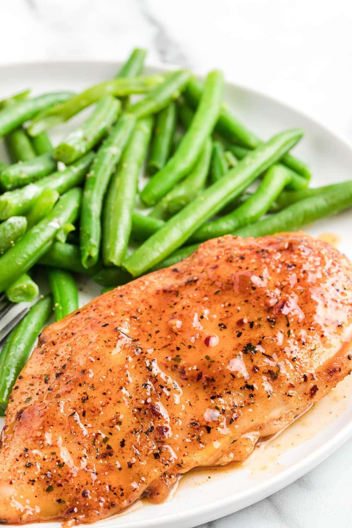 Glazed chicken breast with green beans on a white plate.