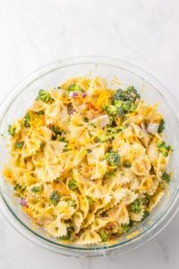 Bowtie pasta salad with broccoli, cheddar cheese, and red onions in a glass bowl.