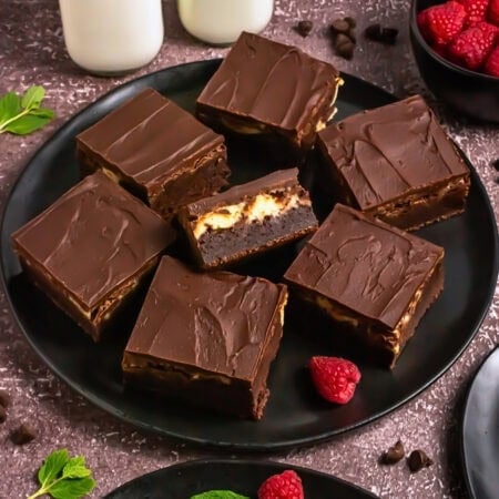Chocolate brownies with a creamy filling on a black plate, garnished with raspberries.