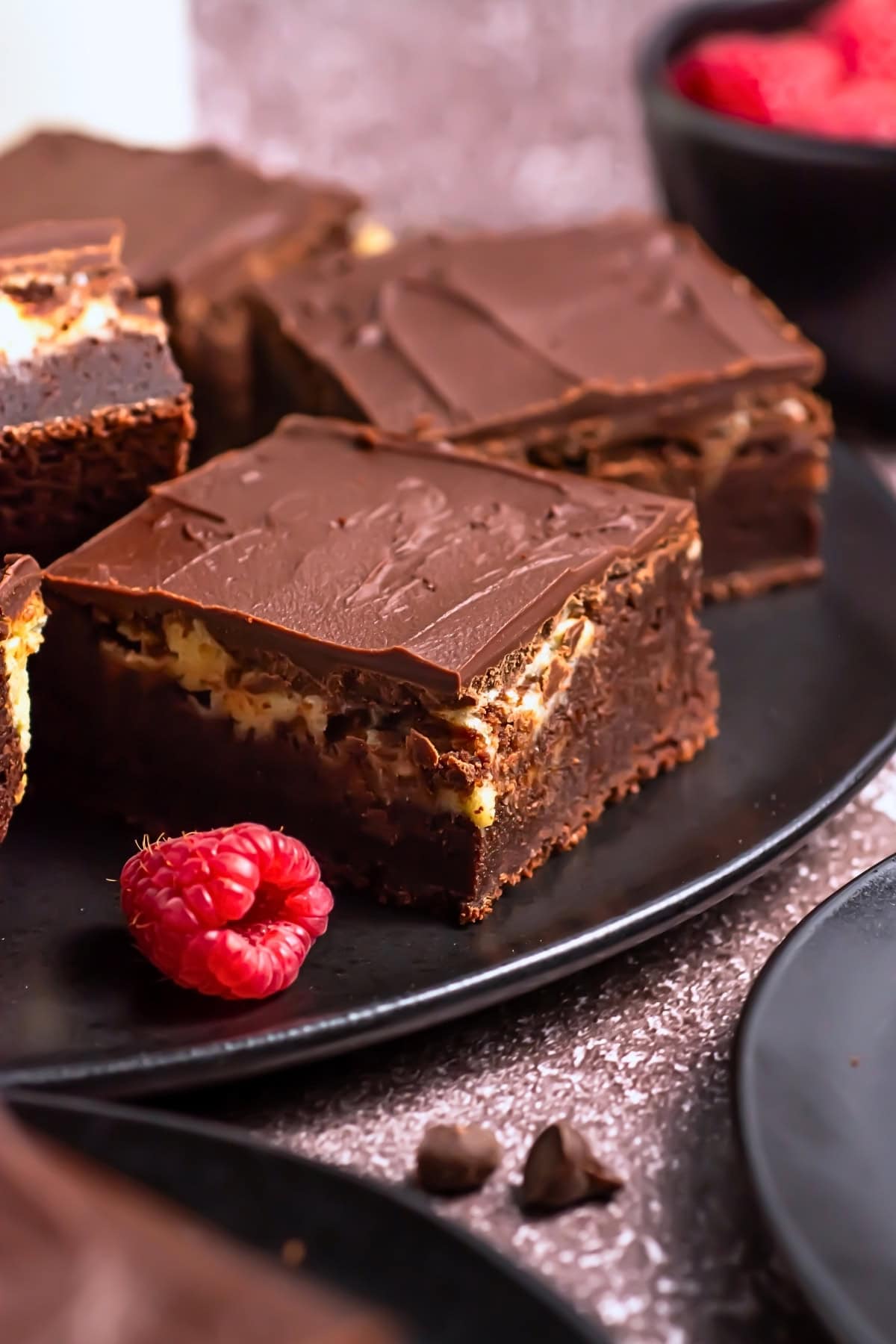 Chocolate brownies with a creamy layer, garnished with fresh raspberries.