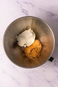 Mixing bowl with cream cheese and peanut butter on a marble surface.