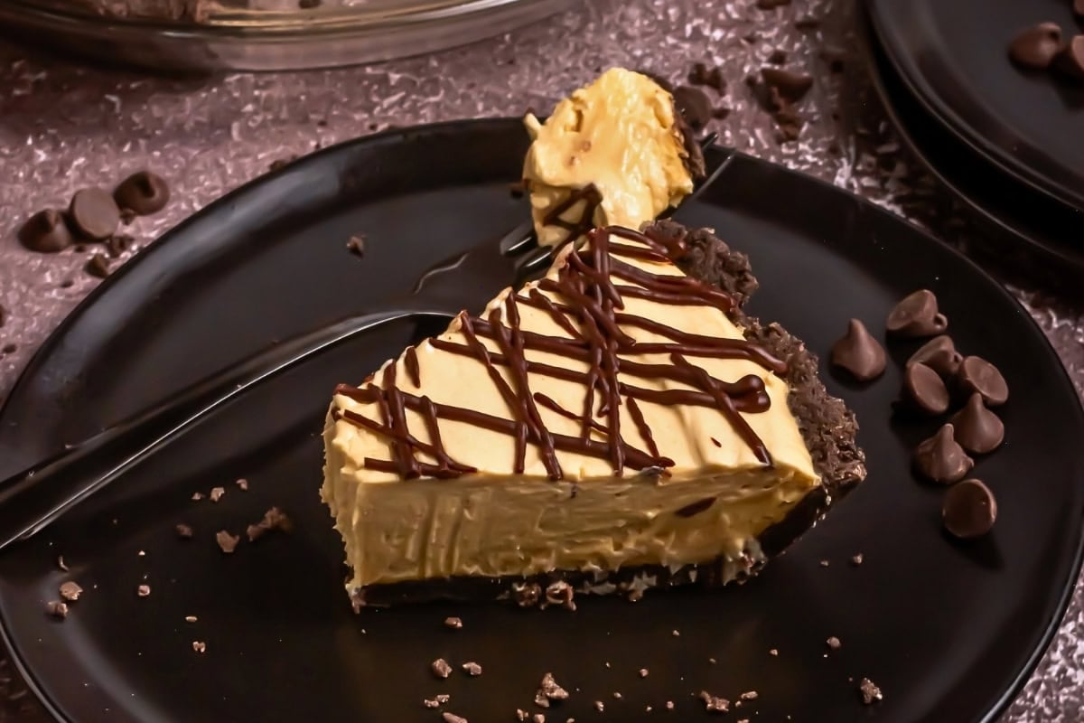 A slice of peanut butter pie with chocolate drizzle on a black plate.