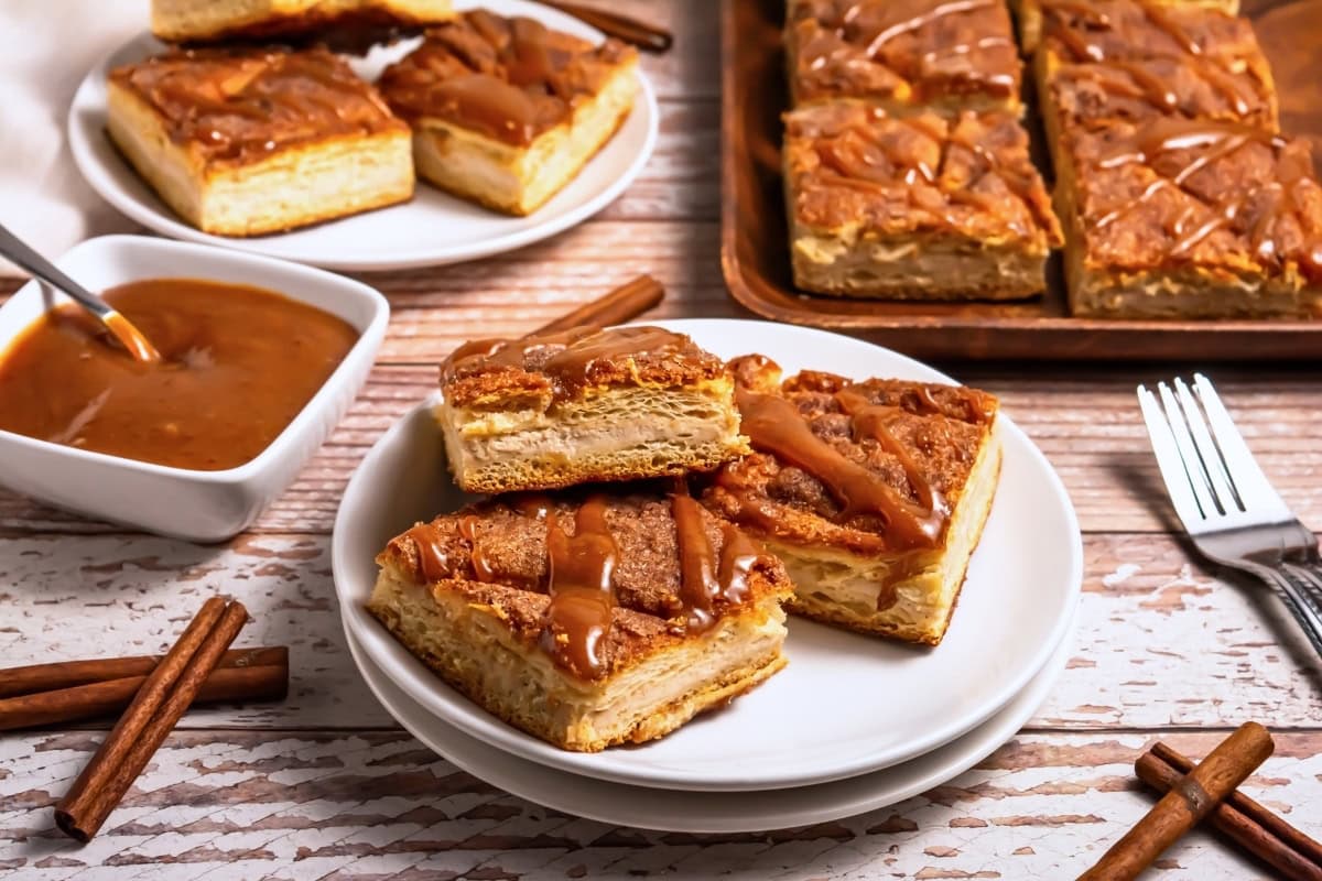 Caramel-drizzled pastry squares on plates with cinnamon sticks and sauce nearby.
