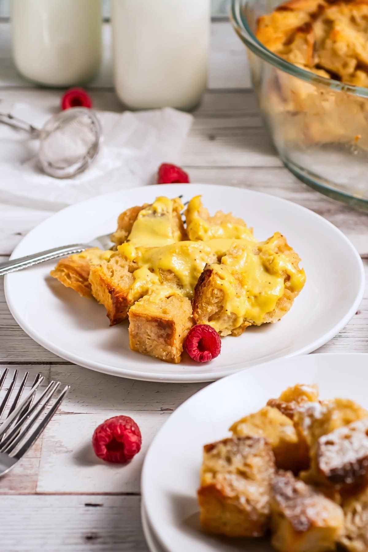 A plate of bread pudding with raspberries and a fork on a white wooden table.