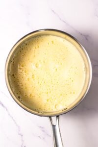 A saucepan filled with frothy, yellow custard on a marble surface.