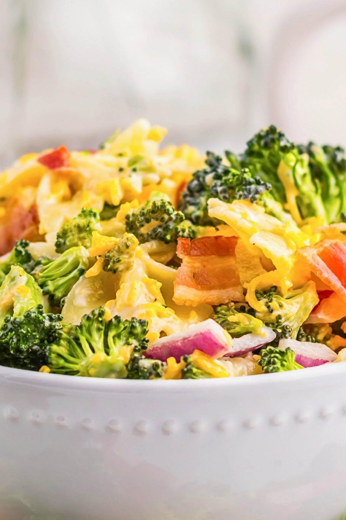 Broccoli salad with bacon, red onion, and shredded cheddar cheese in a white bowl.
