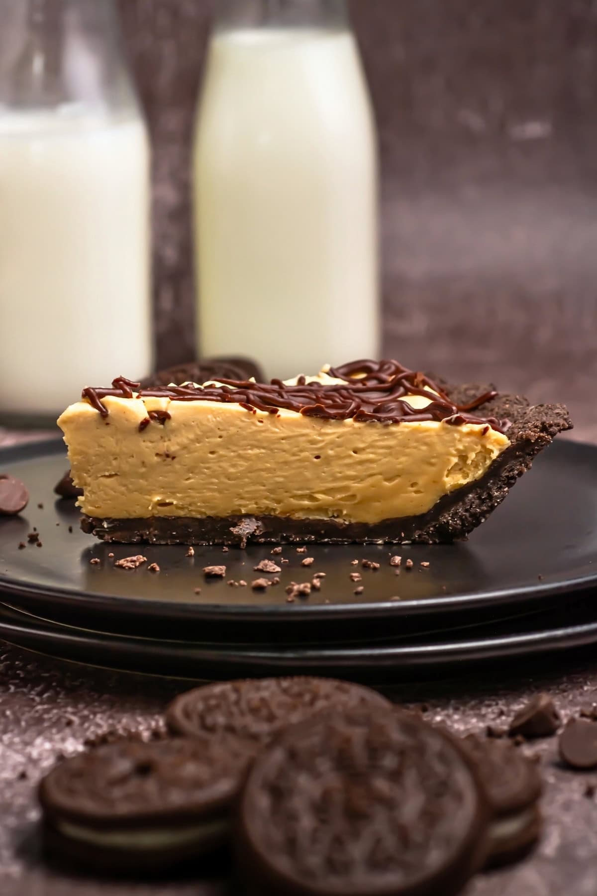 A slice of chocolate peanut butter pie on a black plate with milk bottles.