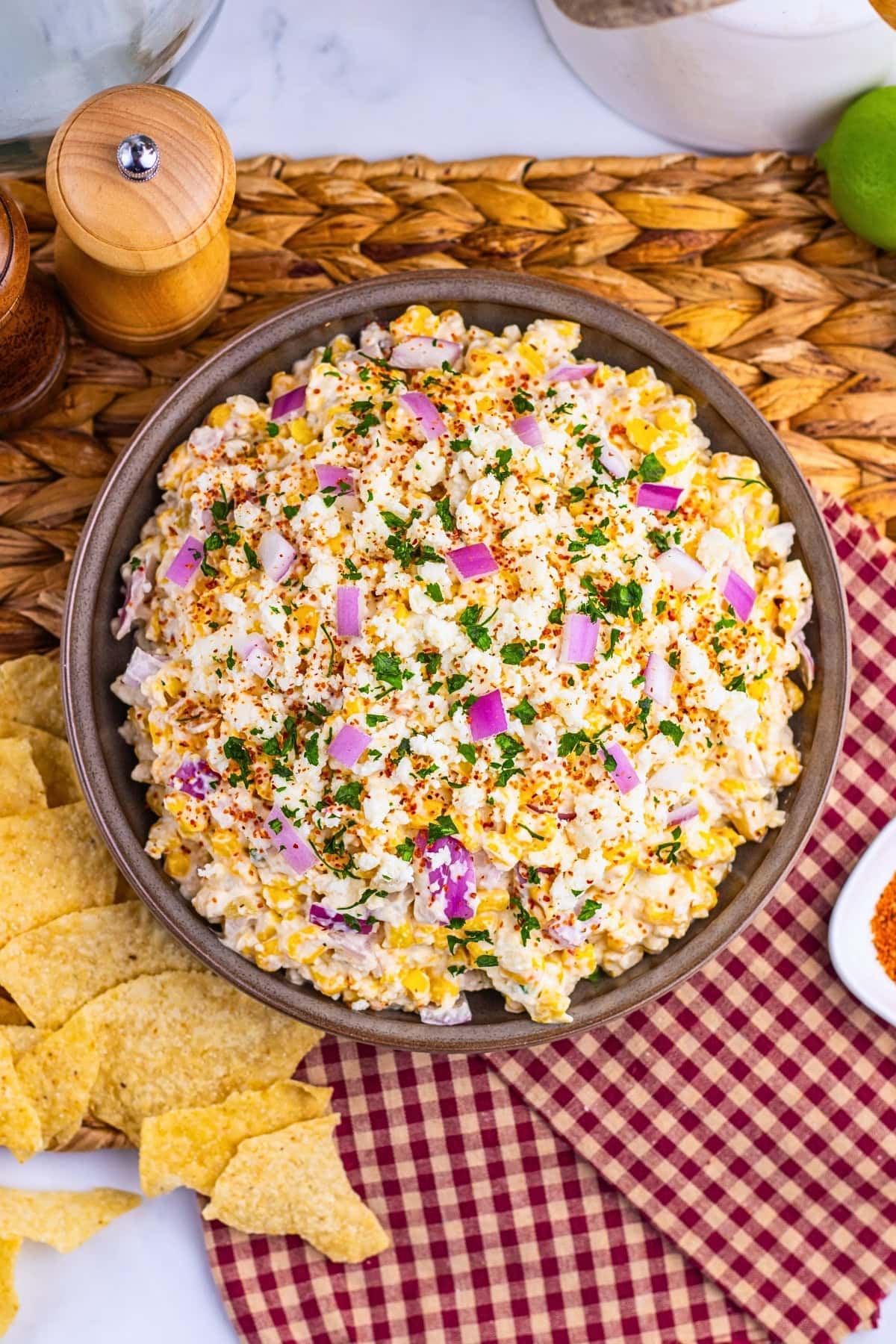 A bowl of creamy corn salad topped with chopped red onions and herbs.
