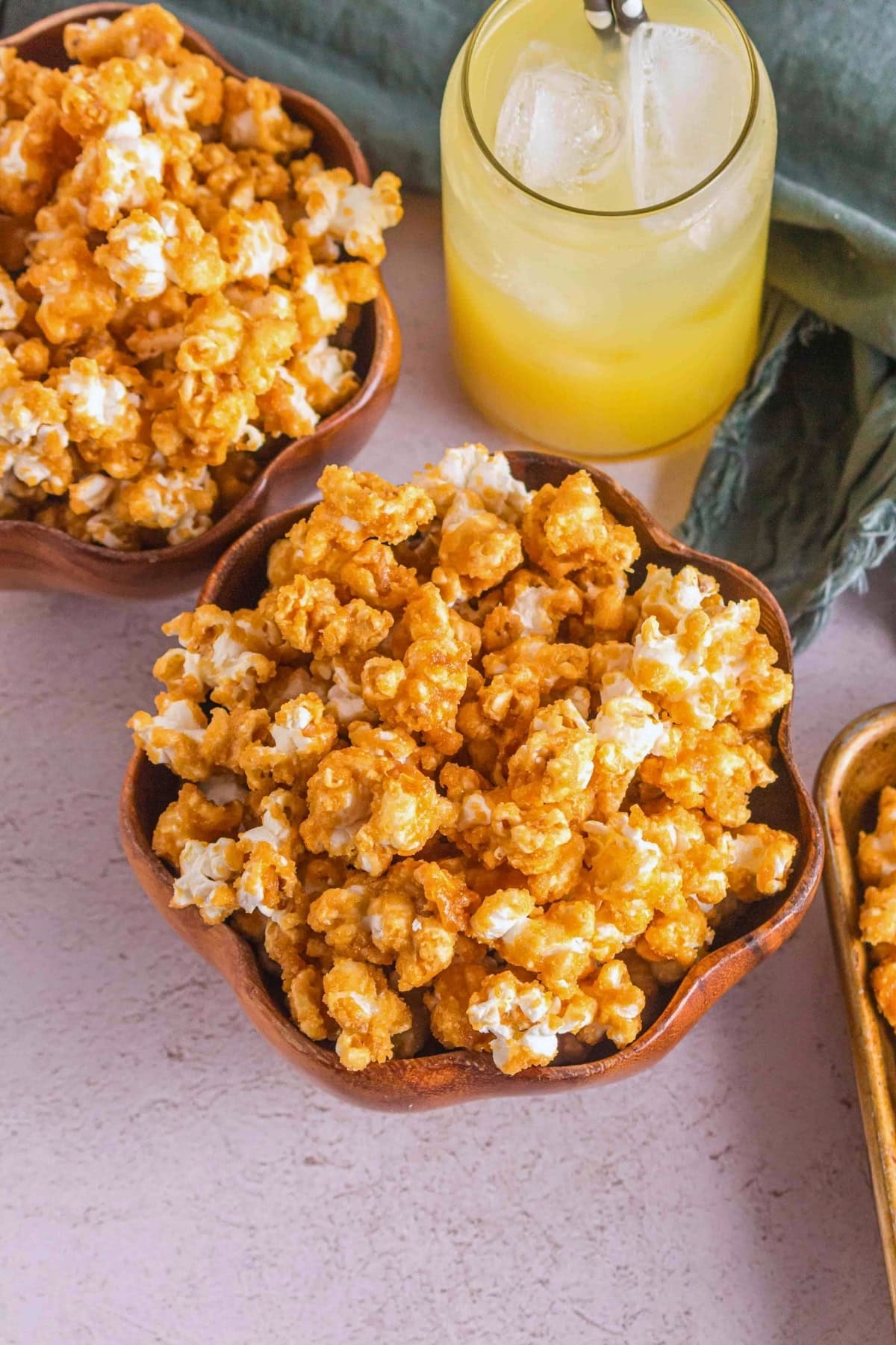 Bowls of caramel popcorn next to a glass of yellow iced drink on a table.