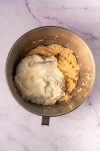 Stainless steel bowl with whipped cream and dough on a marble surface.