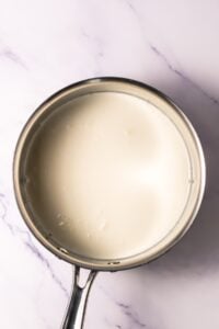 A saucepan filled with a creamy white liquid on a marble surface.