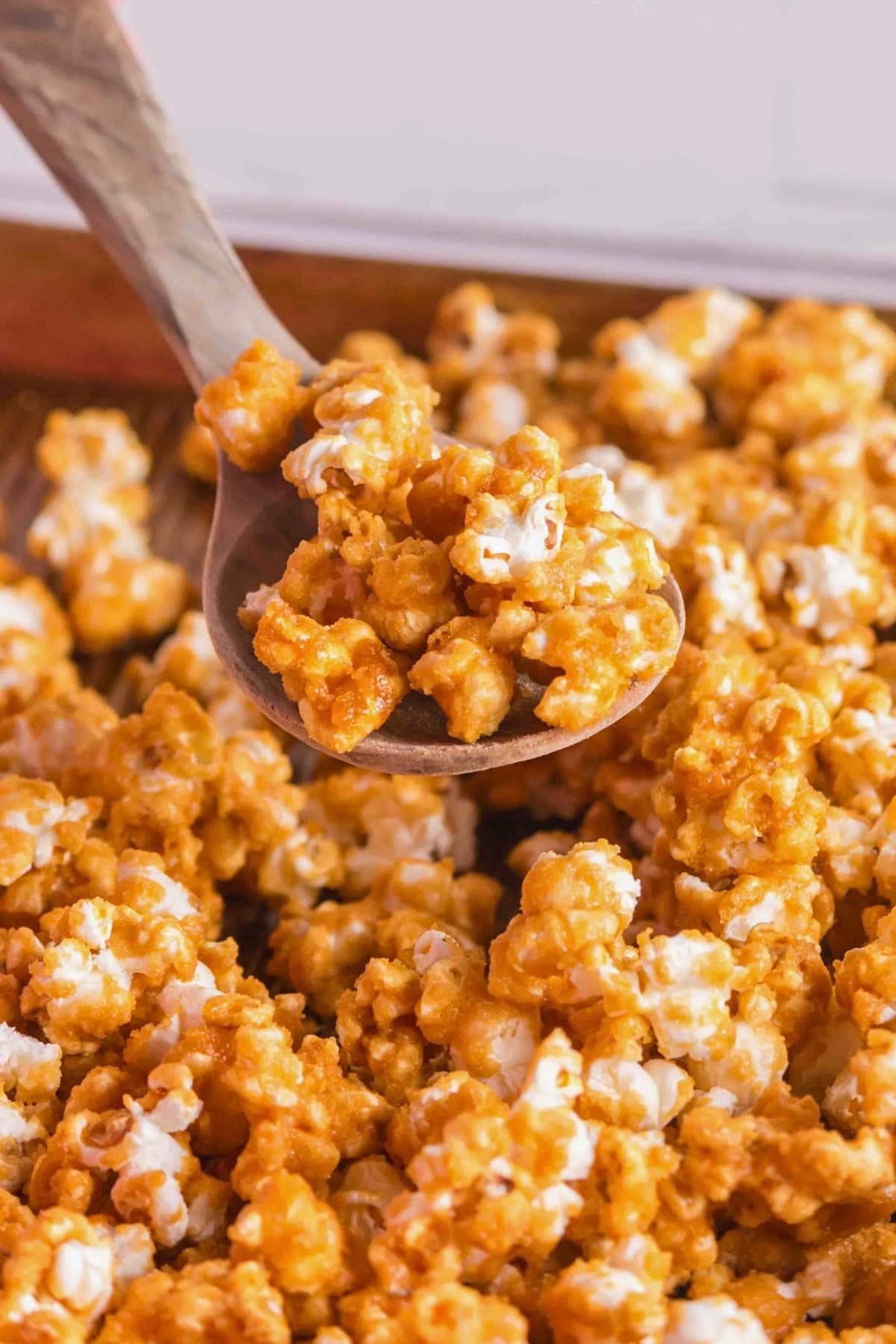 A wooden spoon scoops up caramel popcorn from a pile.