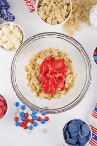 A glass bowl of cereal with red melted candy, surrounded by candy and snacks.