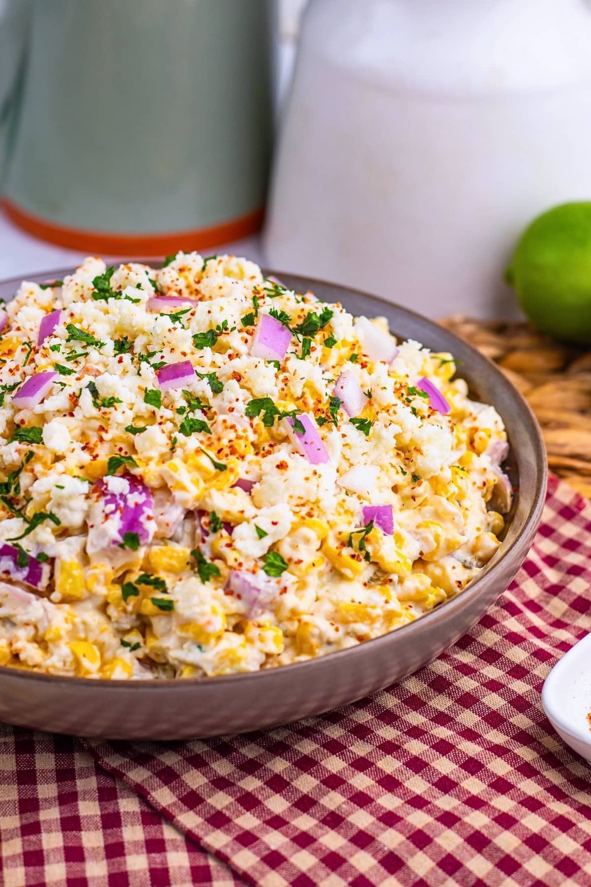 A bowl of Mexican street corn salad with cheese, red onion, and herbs.