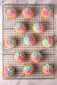 Cupcakes with pink and blue swirled frosting on a cooling rack.