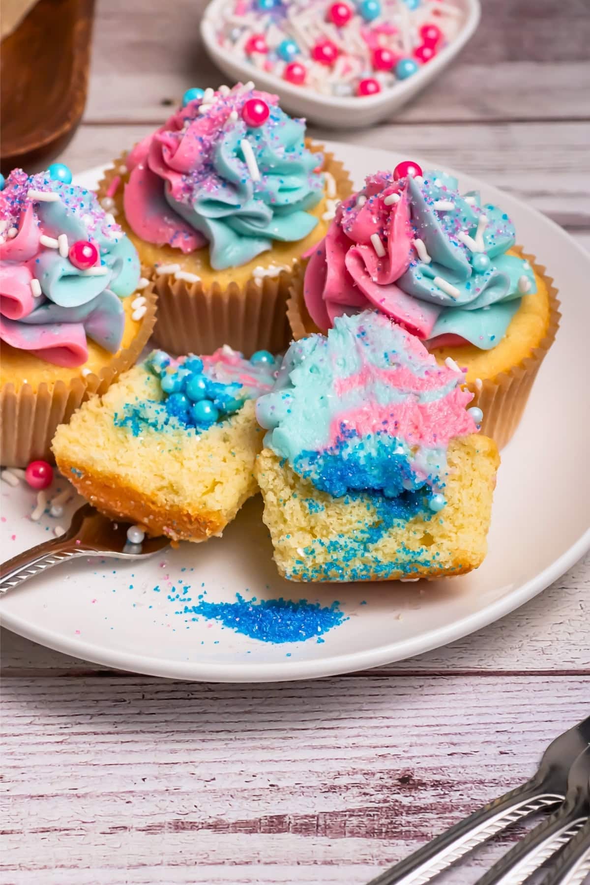Cupcakes with pink and blue swirled frosting and colorful sprinkles on a plate.
