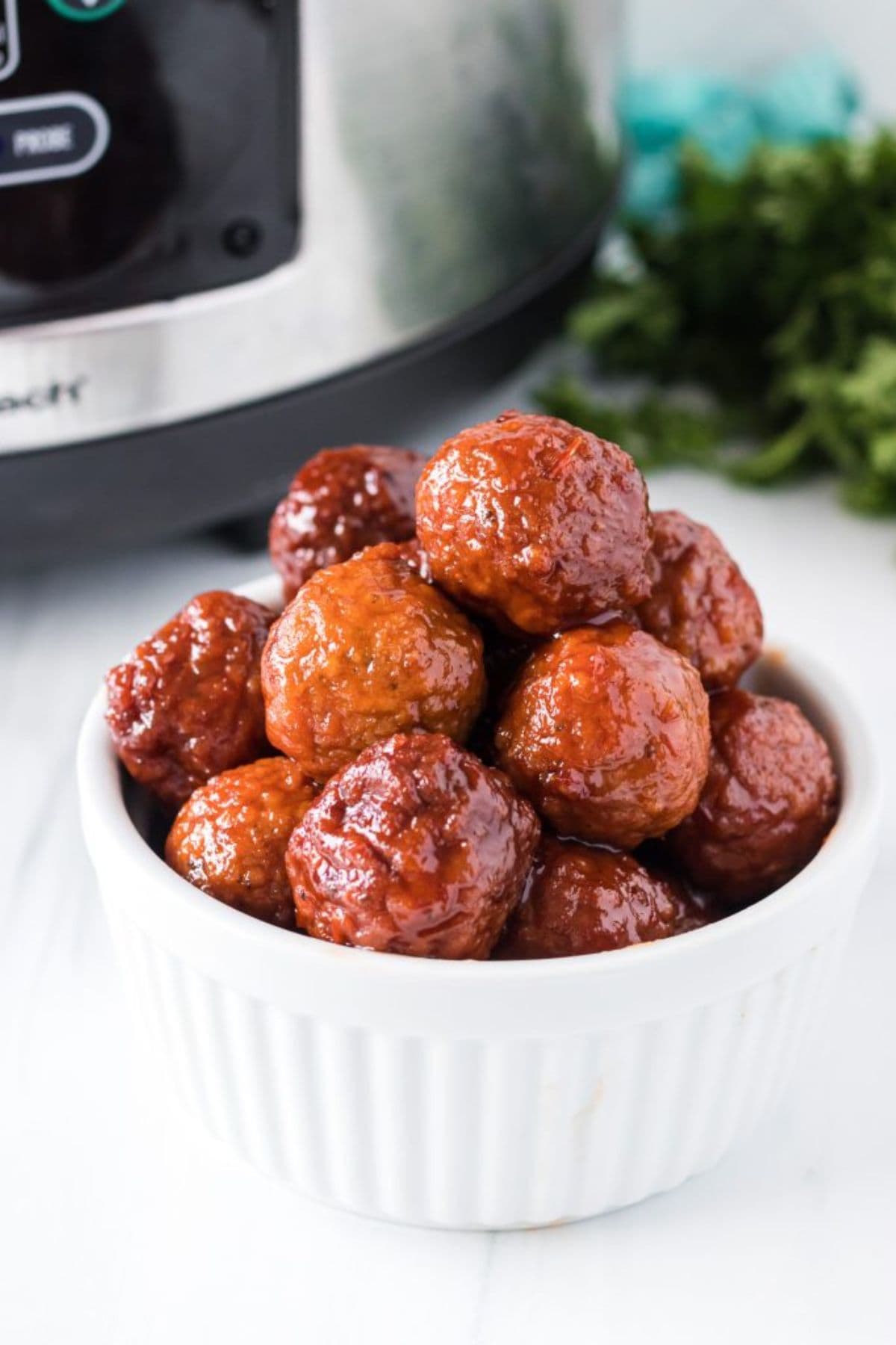 Meatballs in sauce served in a white ramekin near a slow cooker.