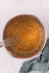 A metal bowl with a whisk mixing a caramel mixture next to a green cloth.