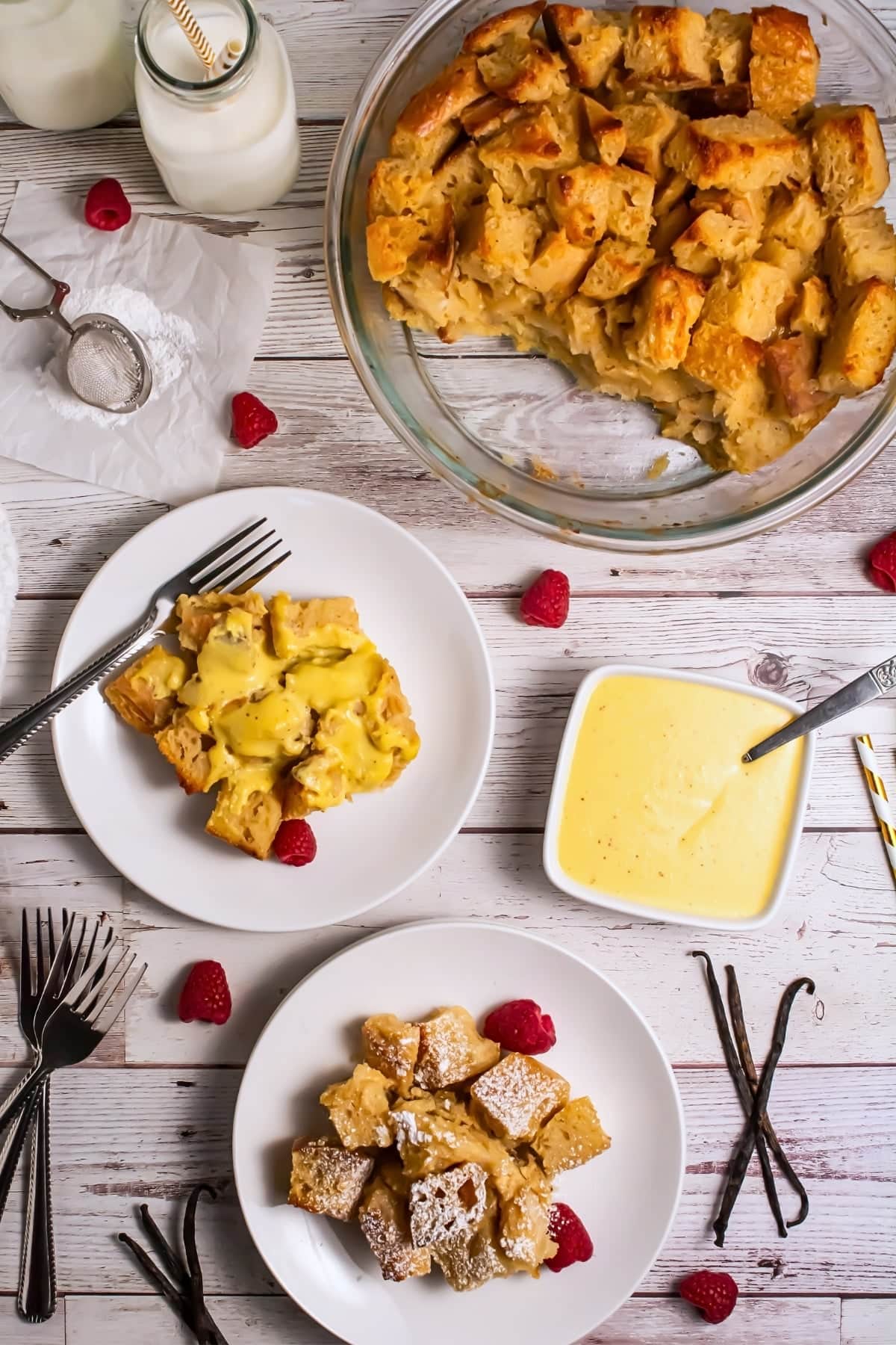 Bread pudding served on plates with vanilla sauce, fresh raspberries, and milk.