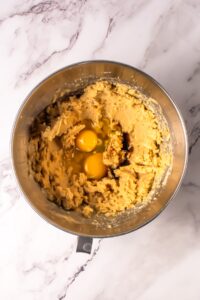 Baking dough in a metal bowl with two raw eggs on top, on a marble surface.