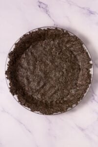 A pie dish filled with a pressed Oreo cookie crumb crust on a marble surface.
