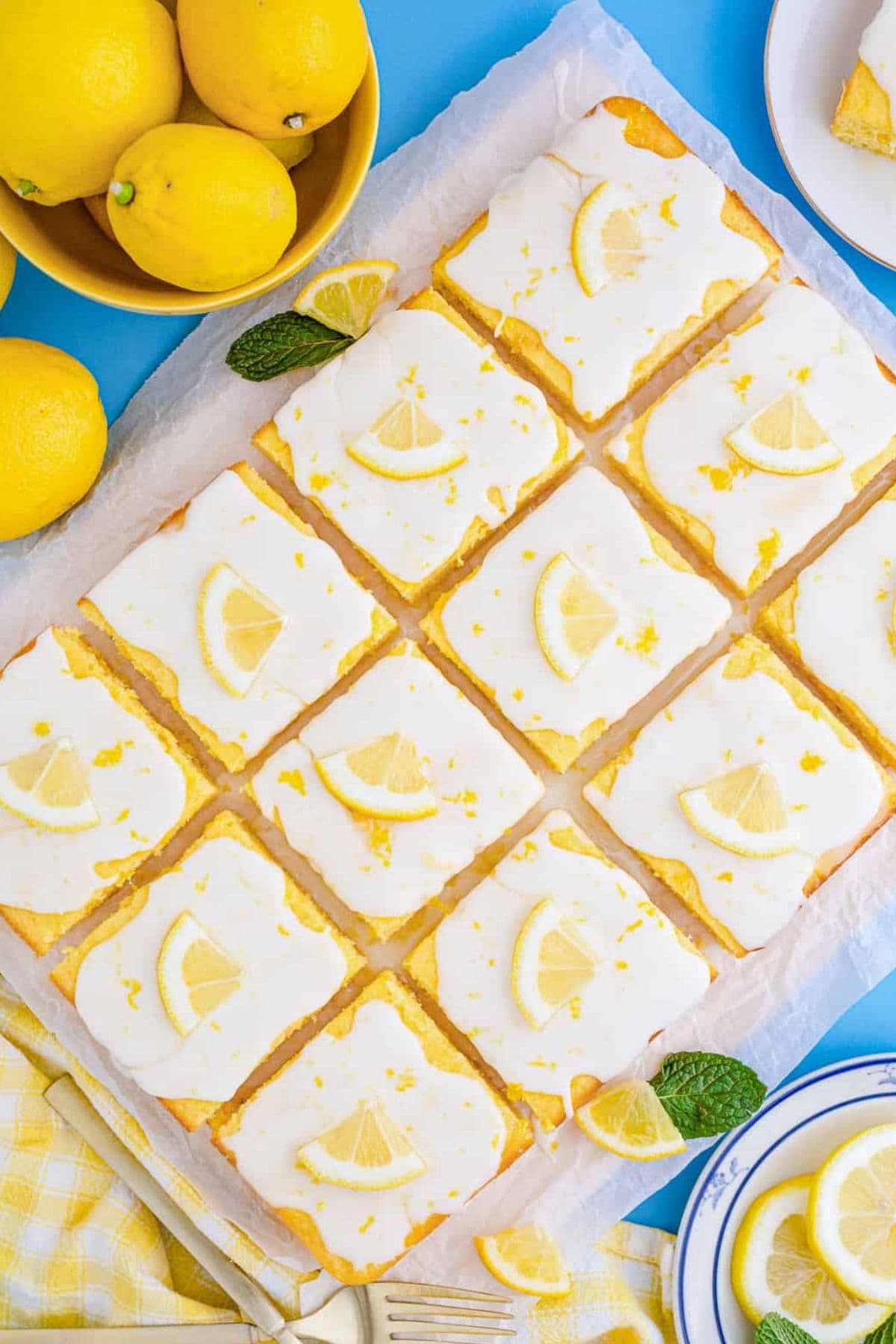 Lemon bars with icing and lemon slices, cut into squares on parchment paper.