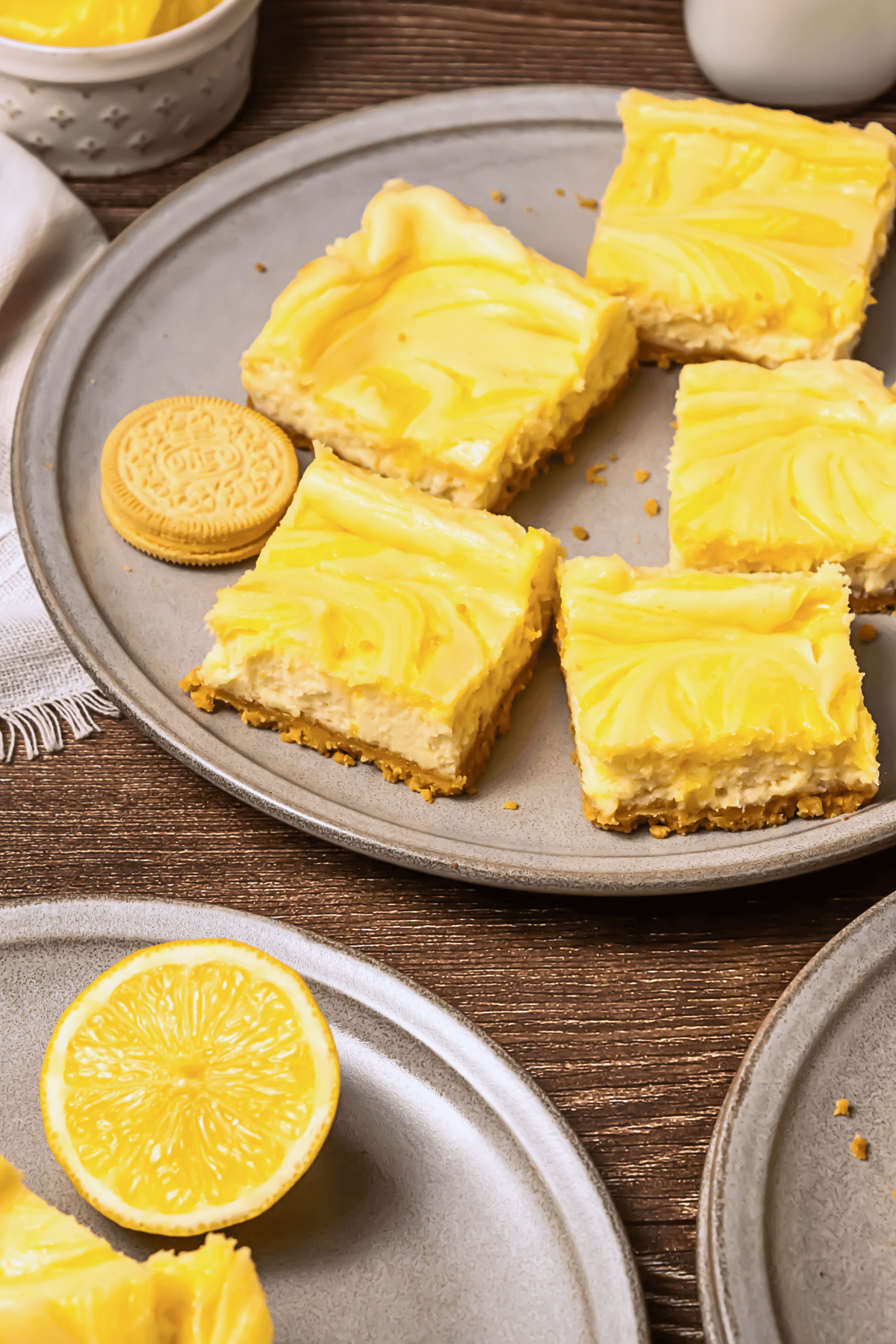 Lemon cheesecake bars on a plate with cookies and a lemon half nearby.