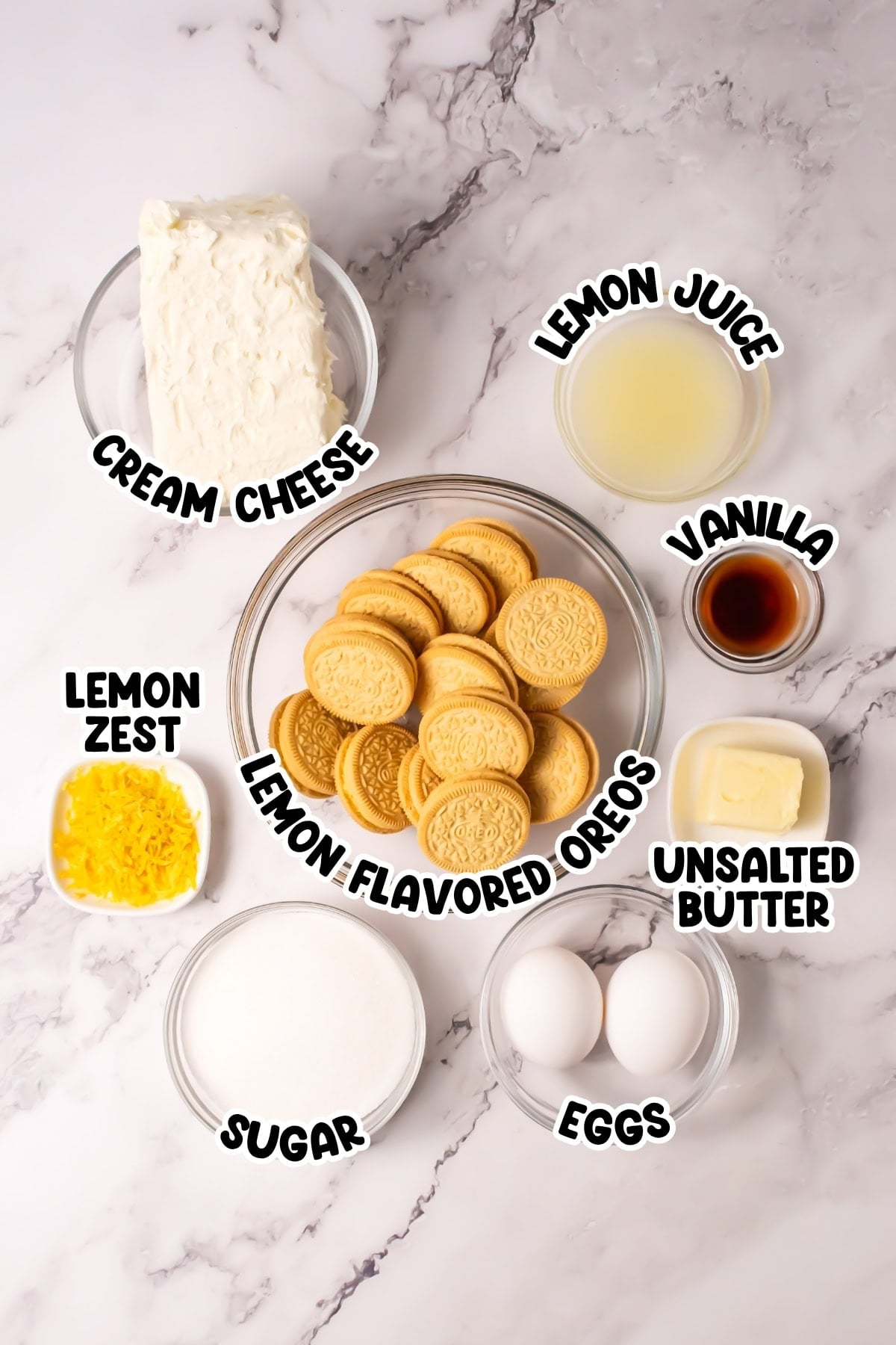 Ingredients for lemon cheesecake laid out in bowls on a marble surface.