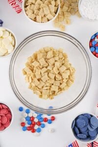 A bowl of Chex cereal surrounded by colorful candies and baking ingredients.