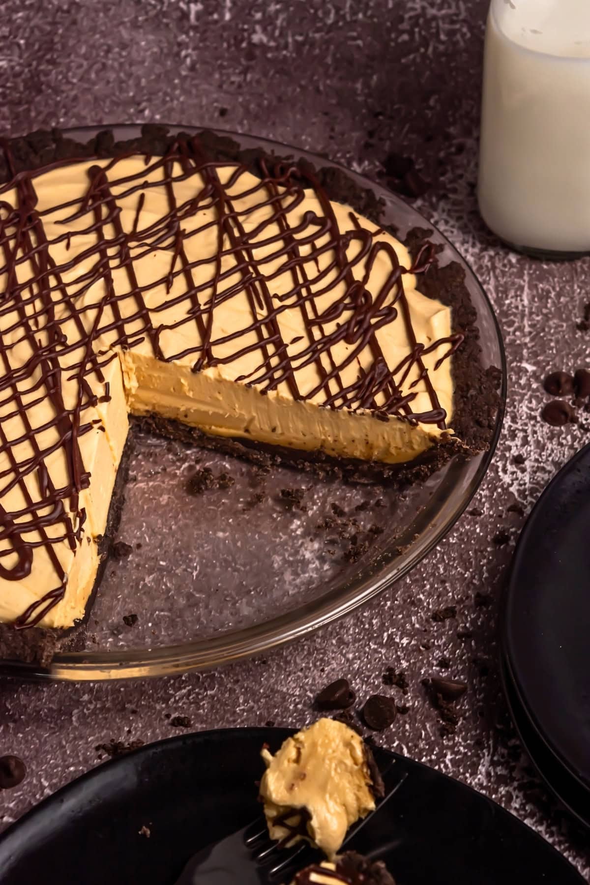 A chocolate-drizzled peanut butter pie with a slice removed, next to milk.