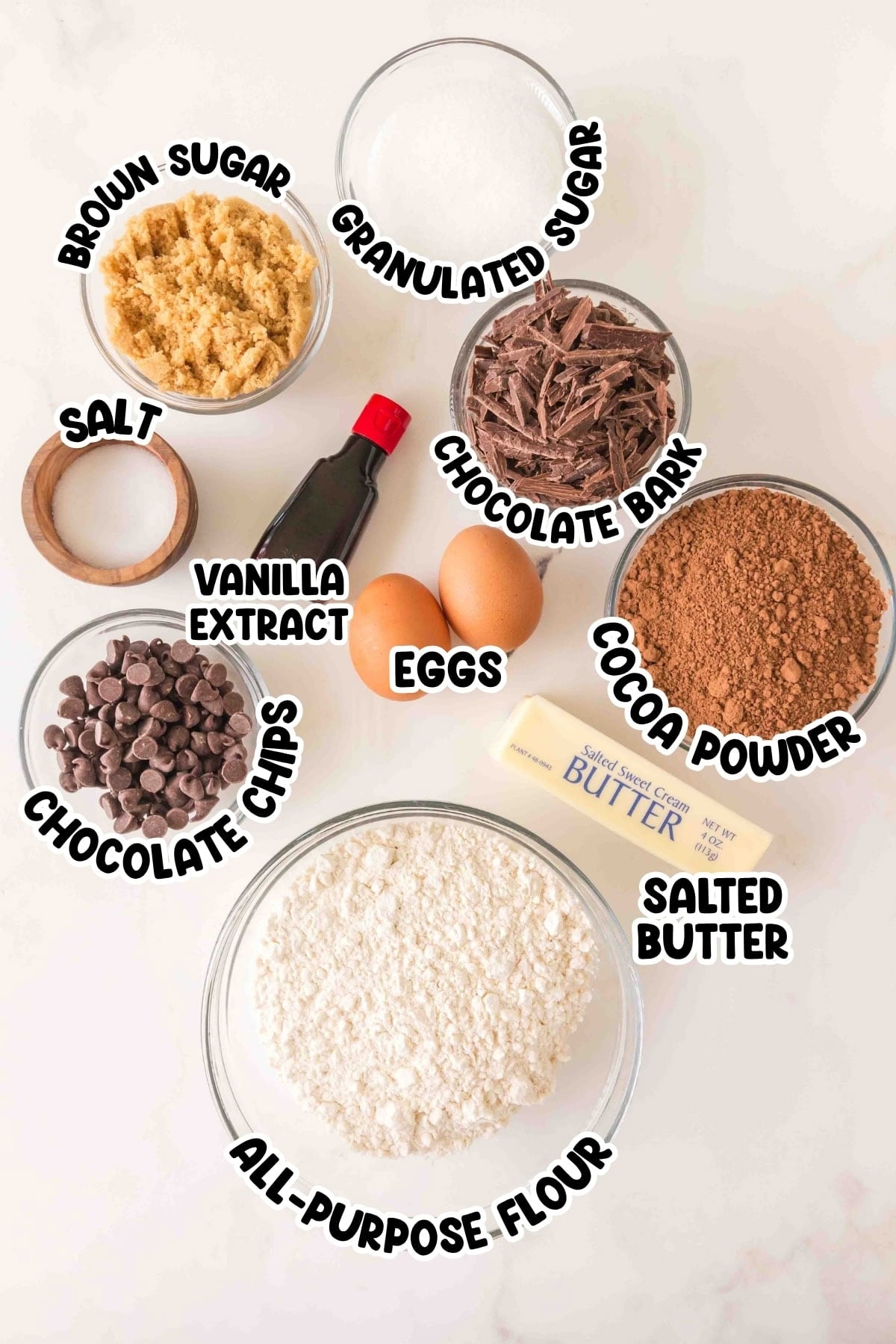 Various labeled baking ingredients in bowls, including sugars, flour, eggs, and chocolate.