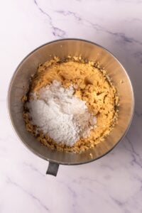 Metal mixing bowl with cookie dough and flour on a marble countertop.