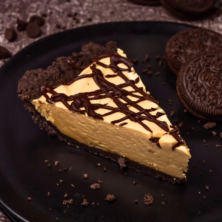 A slice of cheesecake with a chocolate crust and chocolate drizzle on a black plate.