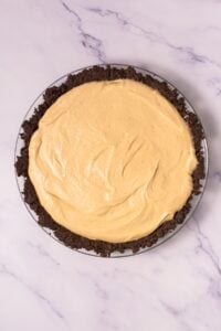 A pie with a creamy light filling and a dark crumb crust on a marble surface.