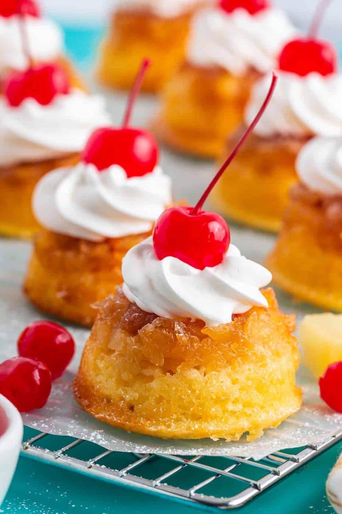 Mini pineapple upside-down cakes topped with whipped cream and cherries.