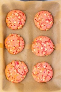 Six pink cookies with white chips and sprinkles on parchment paper.