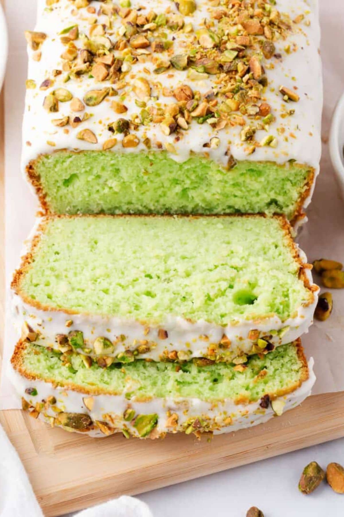 A sliced pistachio loaf cake with white icing and chopped pistachios on top.