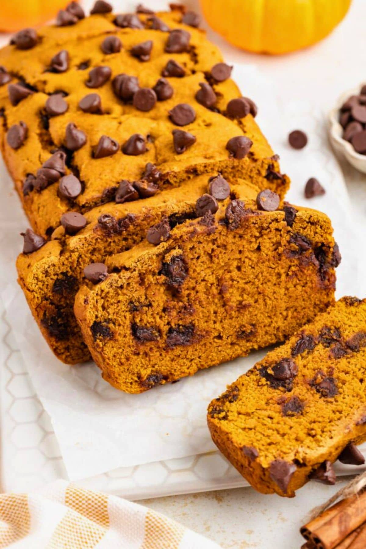 Pumpkin bread loaf sliced, topped with chocolate chips on parchment paper.